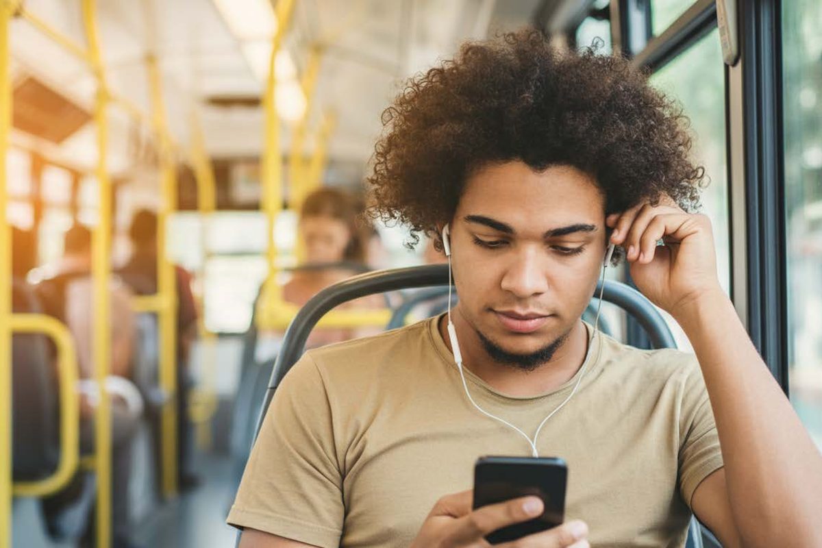 Estudante de fones de ouvido acompanhando o conteúdo pelo celular dentro do ônibus.